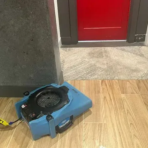 An air mover drying a wood-look tile floor beside an open doorway after a water leak