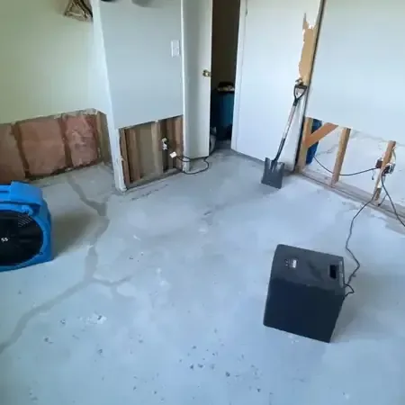 Air movers and a dehumidifier drying a room with the lower drywall cut away and the floor bare