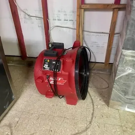 A red air mover running in a room where the lower wall is opened and plastic sheeting is hung